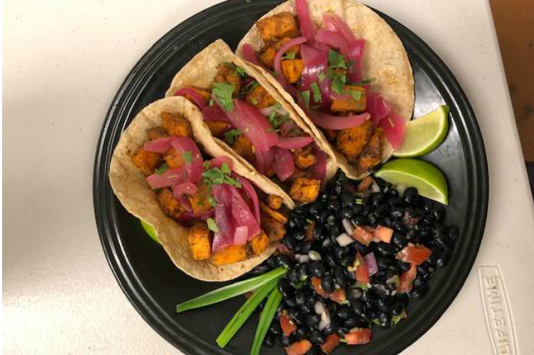 Sweet potato tacos in corn tortillas topped with pickled red onions, with black beans on the side.