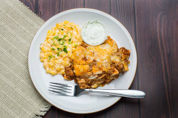 Cheesy ground beef enchilada casserole served with spicy Mexican street corn and lime crema.