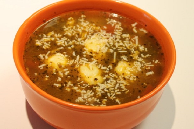 Bowl of spinach tortellini soup with cheese tortellini and vegetables in a savory broth.