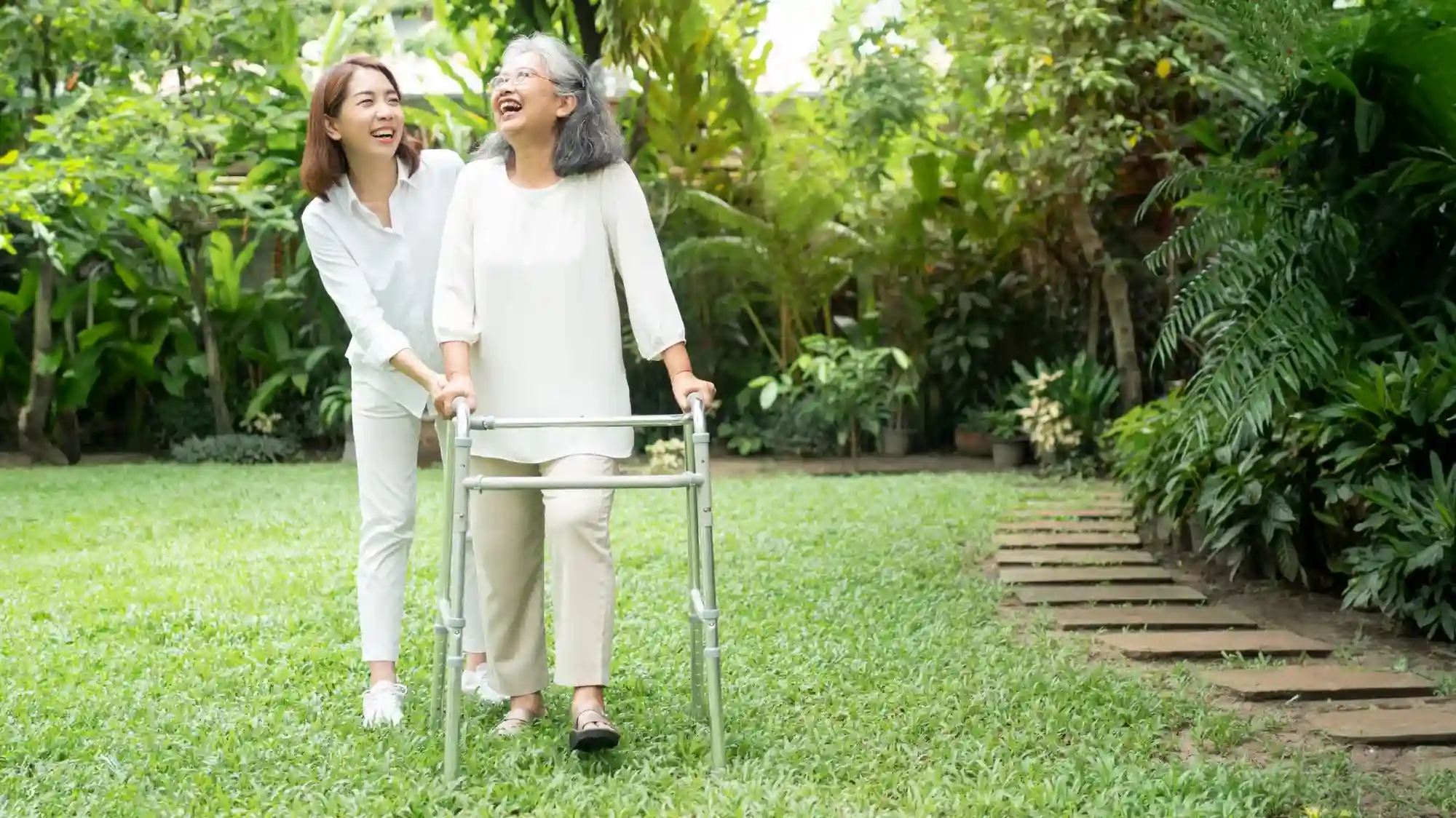 elderly woman walking in the backyard with the assistance of her daughter and a walker