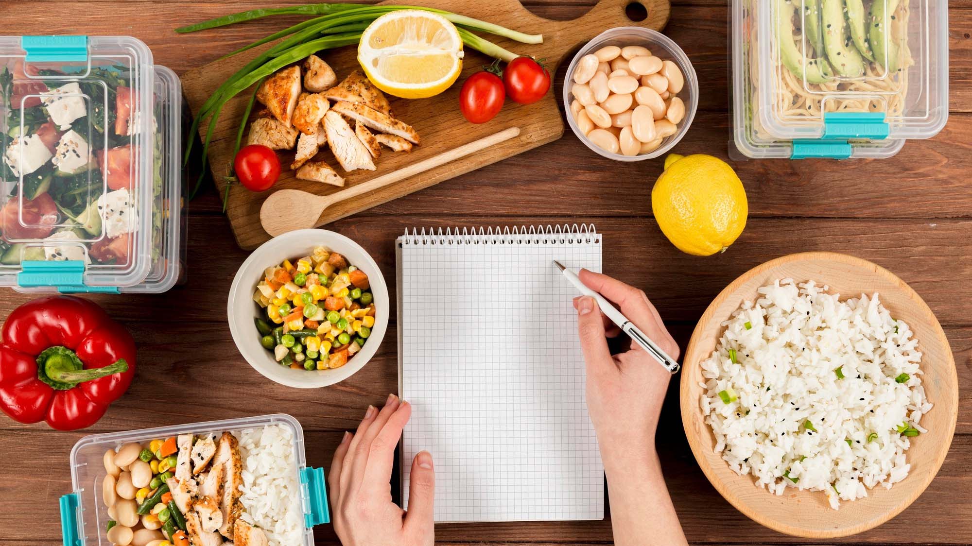 hands-writing-healthy-meal-prep-recipes-on-notebook-with-casseroles-and-food