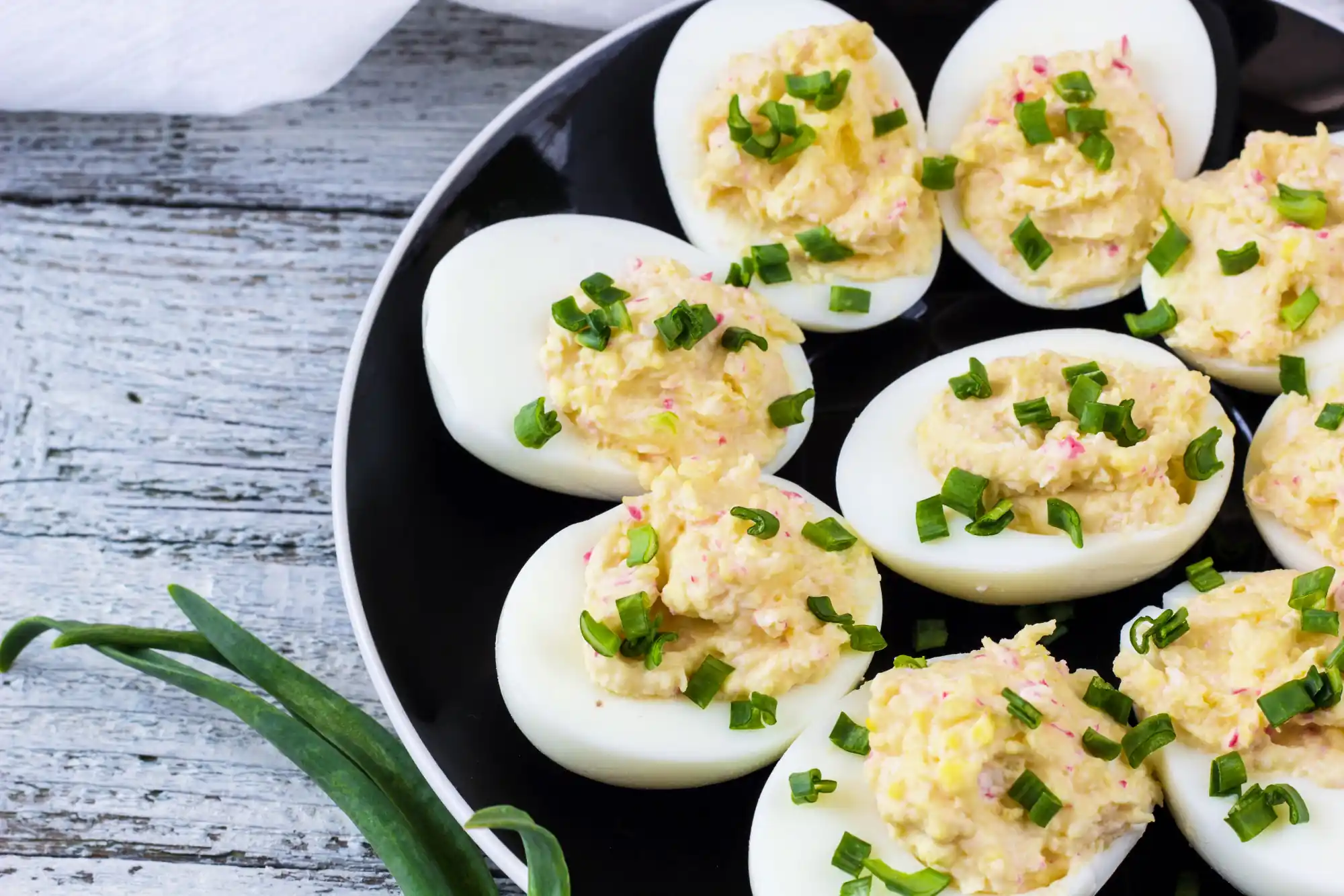 Close-up of deviled eggs topped with finely chopped green onions on a black plate