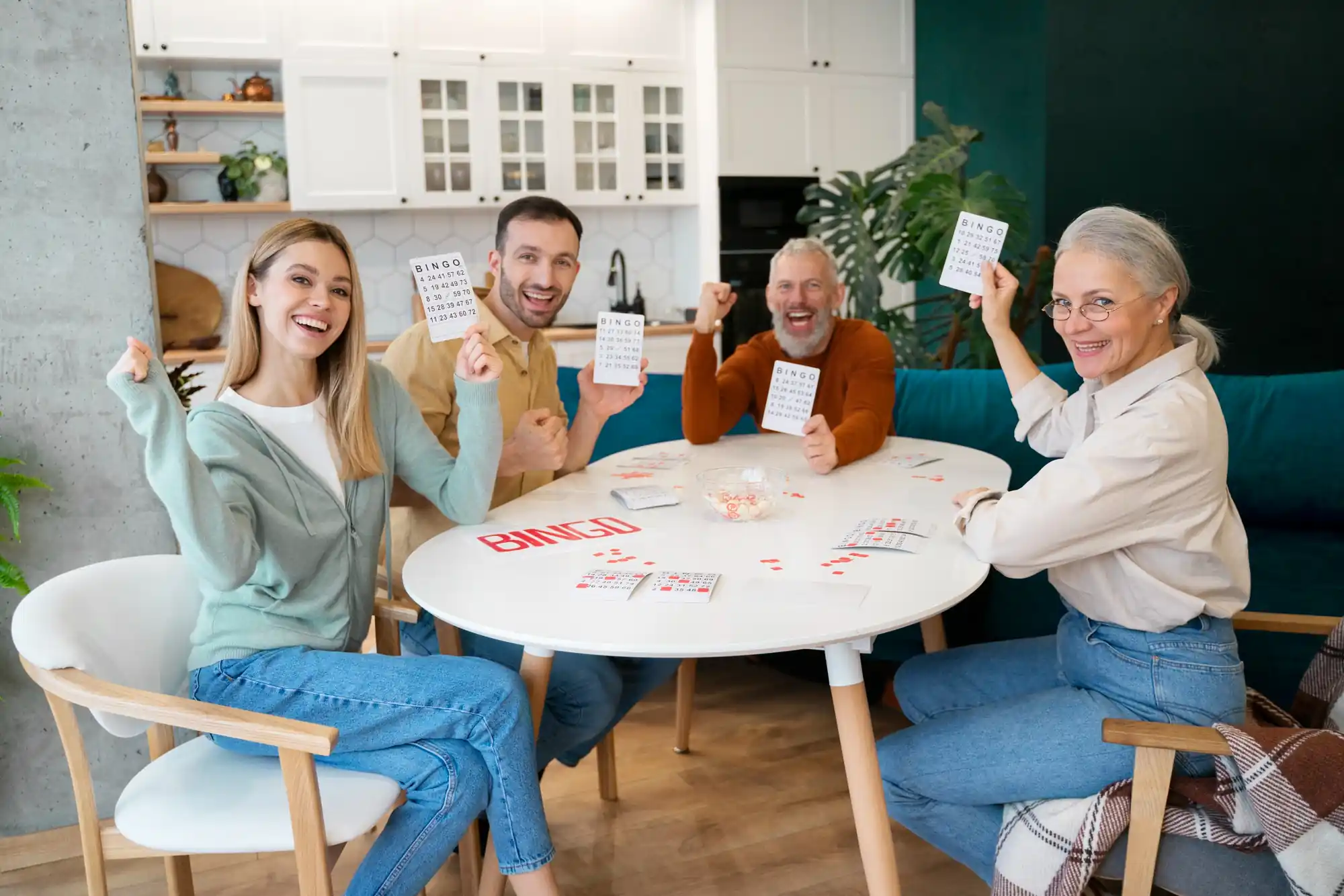 A family of four people of different ages playing bingo around a white table, smiling and proudly holding up their bingo cards