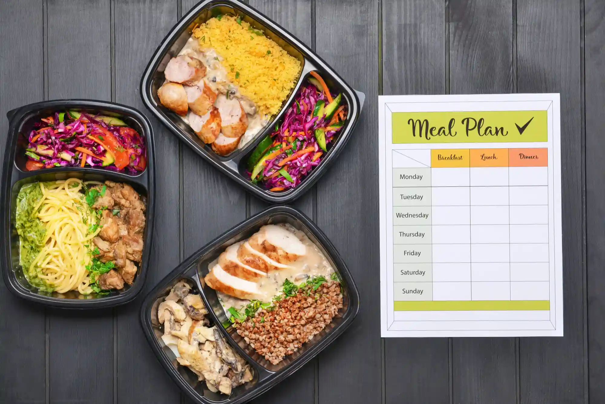 Ready-to-eat meal trays featuring chicken, vegetables, grains, and salads, alongside a daily meal planning sheet